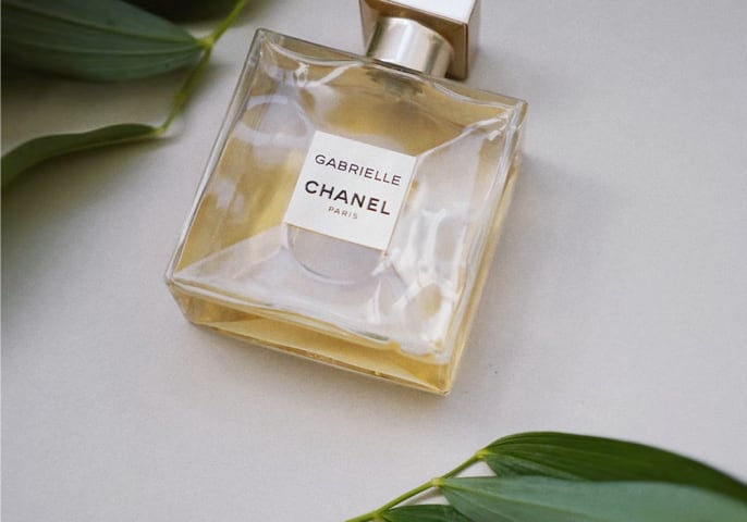 A close shot of an elegant, square-shaped bottle of CHANEL perfume, in either side of which lay some a branch of leaves each